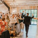 Wedding couple arriving at their wedding breakfast with guests waving napkins.